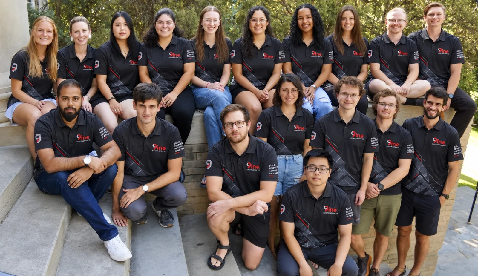A company team sitting on outdoor steps in matching black polo shirts